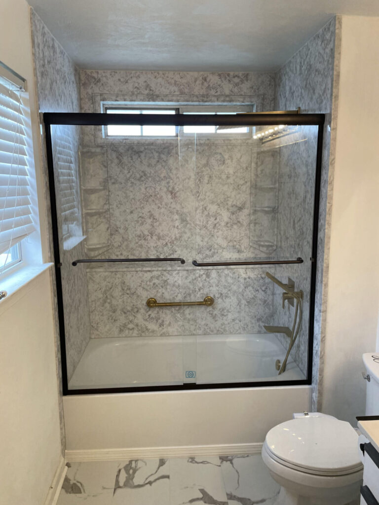 Shower to bathtub conversion with glass doors and a gold grabbar and gold valves